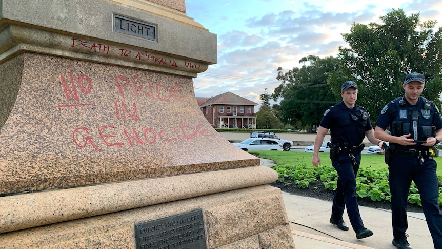 Two police officers walk next to a vandalised statue