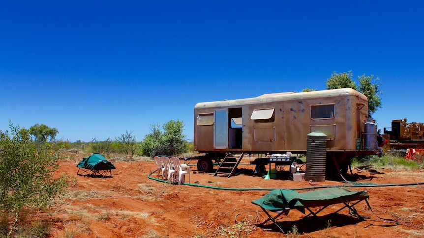 Wide shot of a carvan, bbq, small beds and other items that make up a campsite in the desert