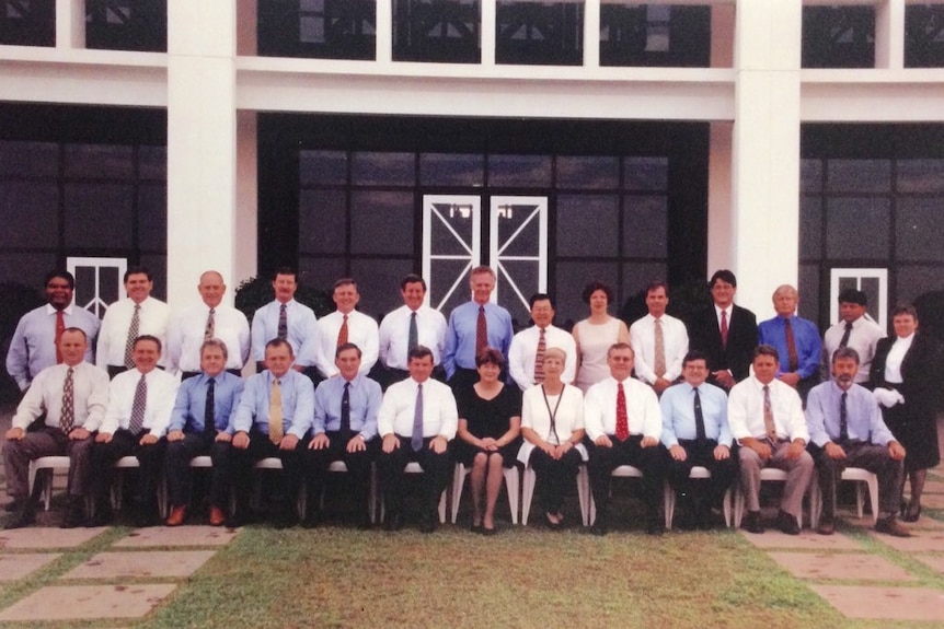 A class photo style of a group of mostly men, formed in two rows.