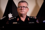NT Police Commissioner Jamie Chalker standing at a lectern and looking up and to the side with a serious expression.