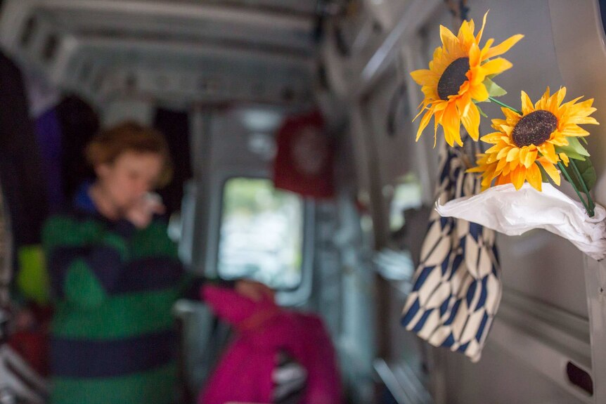Blurred woman in rear of van with plastic sunflowers on right, attached to the van door.