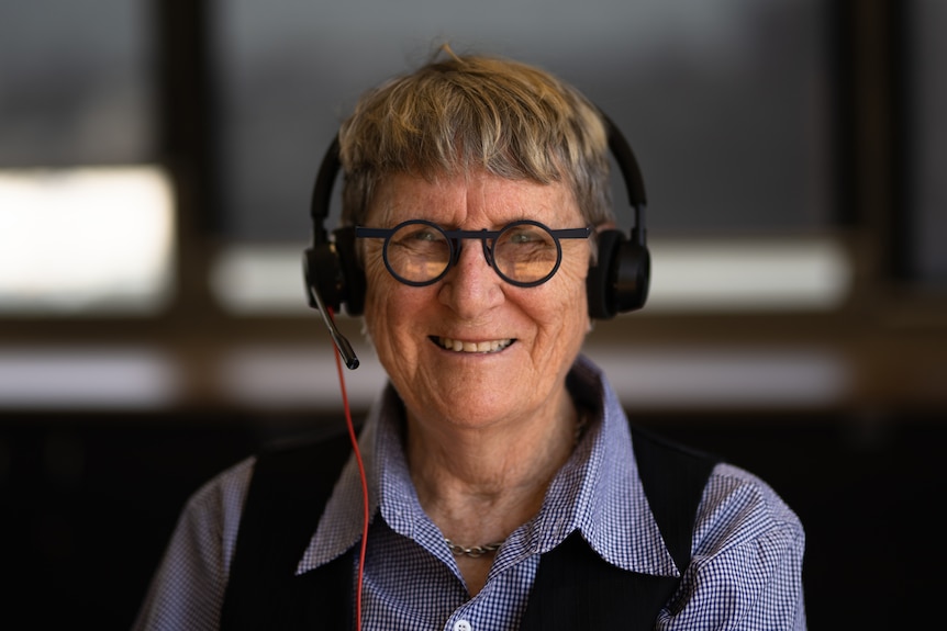 Woman with black glasses and a blue shirt taking a call with headphones.