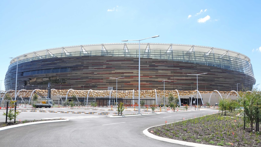 A wide shot of the exterior of the new Perth Stadium with a car park and garden beds in the foreground.