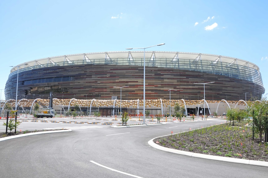 A wide shot of the exterior of the new Perth Stadium with a car park and garden beds in the foreground.