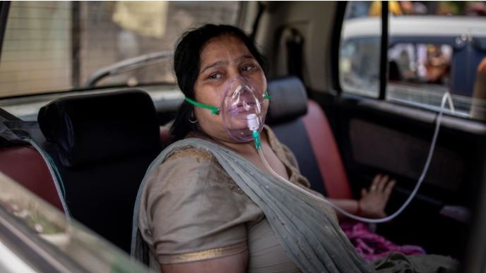 Indian woman sits in back seat of a car with an oxygen mask on her face