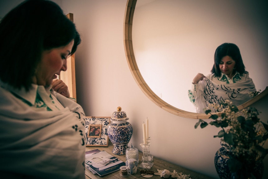 A woman standing in front of a mirror wears a white sheath over a dress printed with Arabic letters