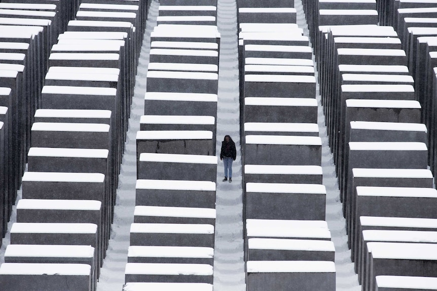 A woman stands among the concrete columns of the Berlin Holocaust memorial after heavy snowfall.