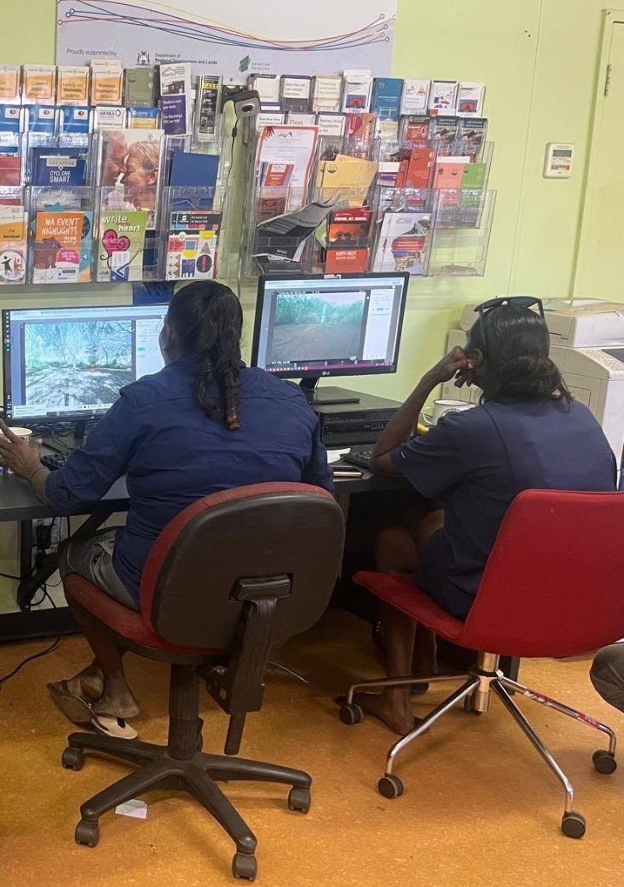 Two dark-haired women sitting side by side in an office, looking at computer screens.