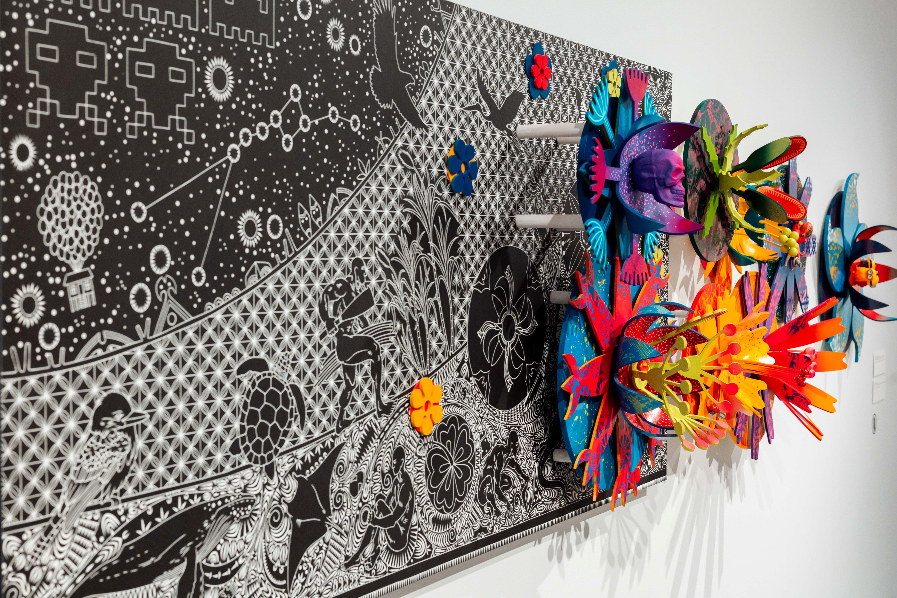 A black and white lino-cut adorned with colourful flower-like sculptural elements.