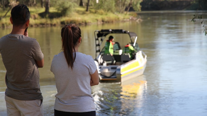 Two people wait on the river bank for news of a missing loved one