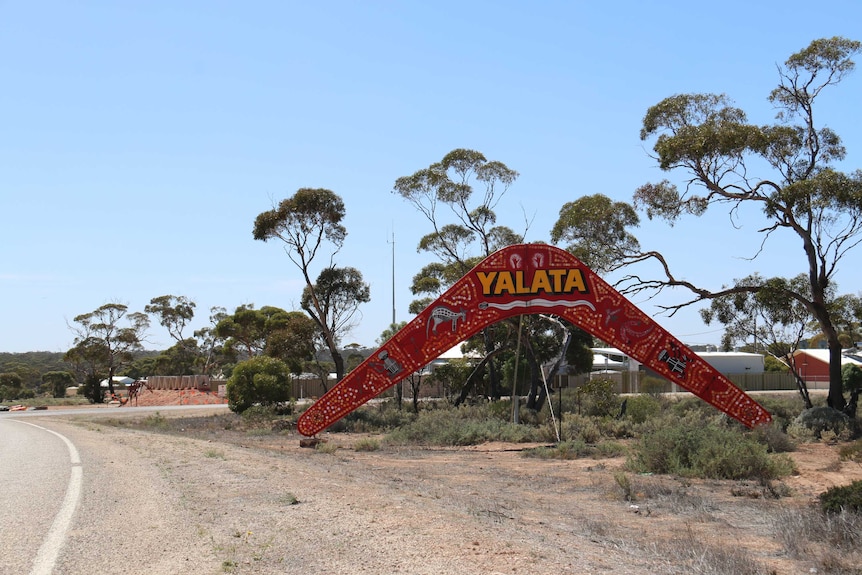 Large boomerang welcome sign with indigenous painting saying Yalata near road.