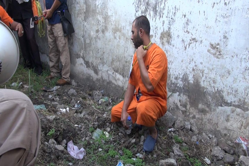 Prisoner Sayed Mohammed Said crouches on his knees next to a white wall.
