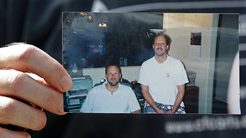 A man's hand holds a photograph of two middle-aged men.