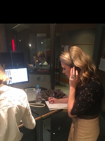 Rachael Brown wearing headphones and taking notes while talking to a telephone caller in radio studio.