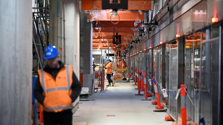 Construction workers stand along a train platform. 