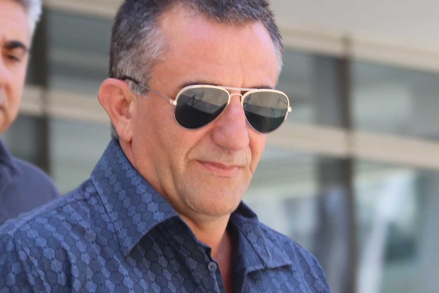 A man in a blue shirt and sunglasses outside court.