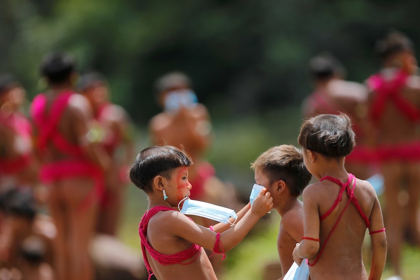 A child from the indigenous Yanomami ethnic group holds a protective face mask to another child.