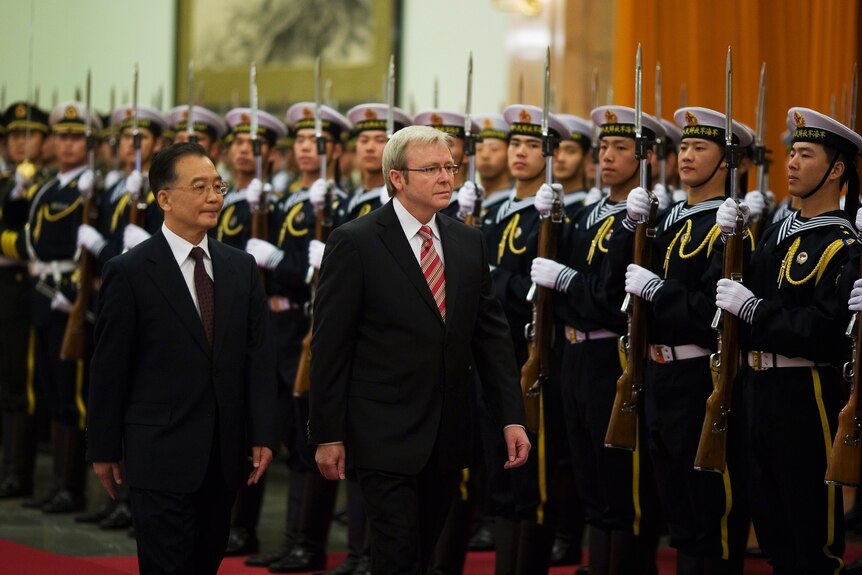 Kevin Rudd walks past lines and lines of Chinese soldiers holding guns.
