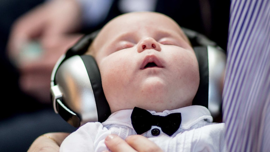A sleeping baby with a bow-tie and headphones on.