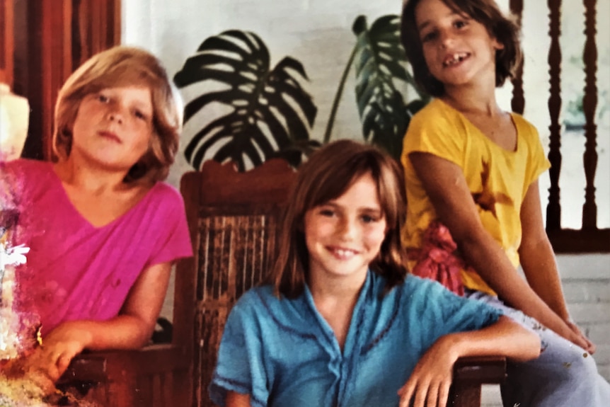 A 1980s colour photograph of a boy in a pink shirt, another in a yellow shirt and a seated girl in a blue shirt