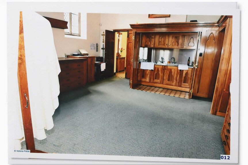 A photograph showing the interior of a priest's sacristy, with a timber panelled kitchenette and robes hanging on a rack.