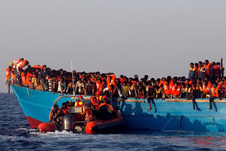 A rescue boat approaches an overcrowded wooden vessel with migrants from Eritrea, off the Libyan coast in Mediterranean Sea.