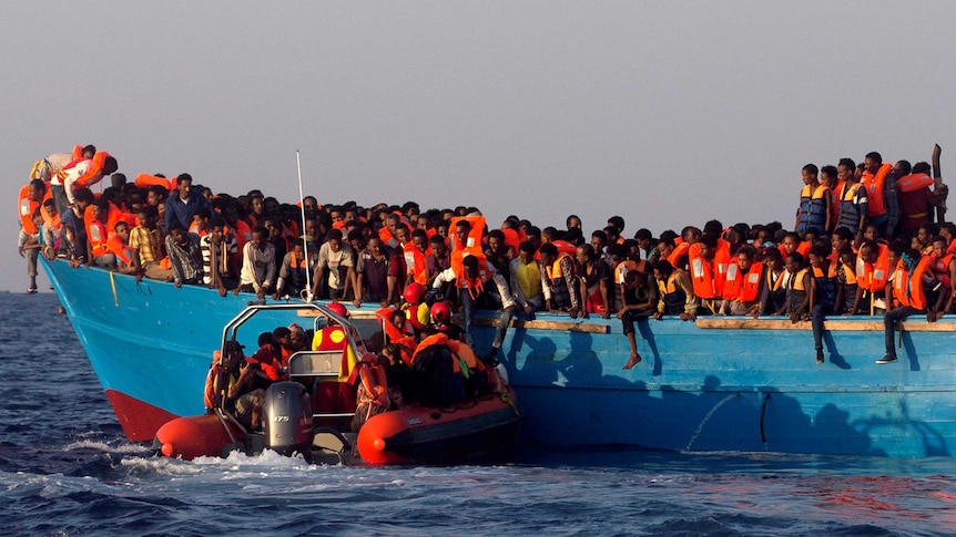 A rescue boat approaches an overcrowded wooden vessel with migrants from Eritrea, off the Libyan coast in Mediterranean Sea.