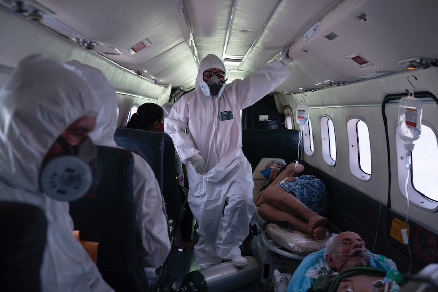 a person in a hazmat suit walks between stretchers of ill people inside a plane.