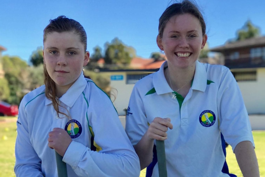 Junior cricketers Grace and Nell Bryson-Smith kneel with cricket bats.