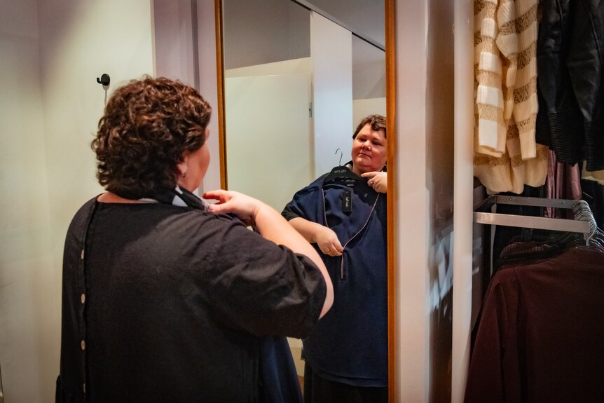 Heidi Arntzen holds up a top as she looks at herself in the mirror in a clothes shop.