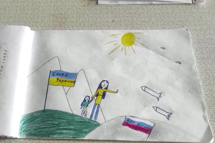 A child's drawing shows a woman and girl standing on a hillside next to a Ukrainian flag, holding up hands to block missiles.