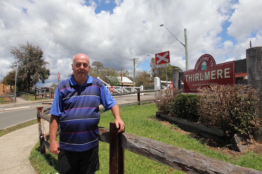 A man standing outside, leaning against a fence.