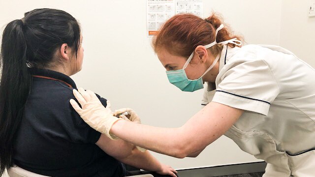 Pharmacist in a mask administering a flu vaccination to a woman