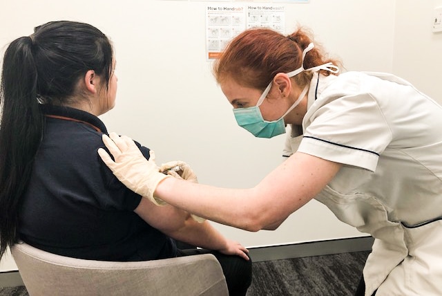 Pharmacist in a mask administering a flu vaccination to a woman
