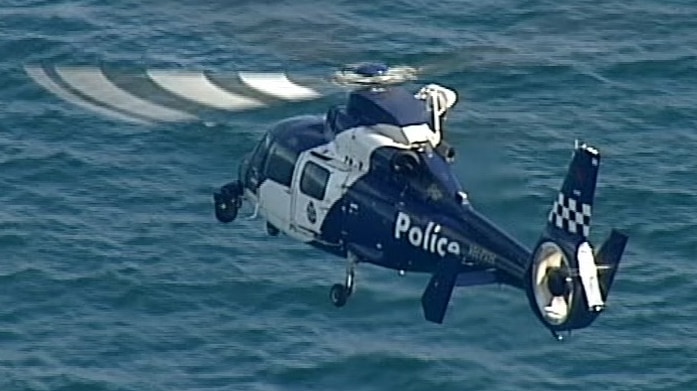A blue police chopper hovers over blue water.