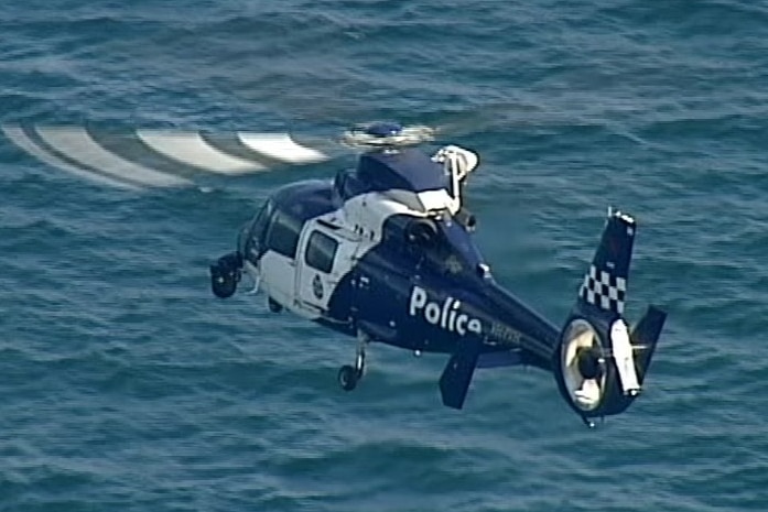 A blue police chopper hovers over blue water.