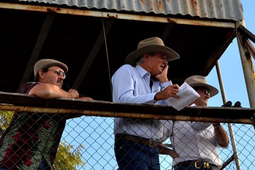 Three men wearing hats in a racing callbox.
