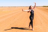 A dancer stands, poised, on a red dirt road.