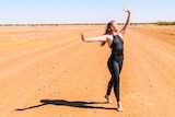 A dancer stands, poised, on a red dirt road.
