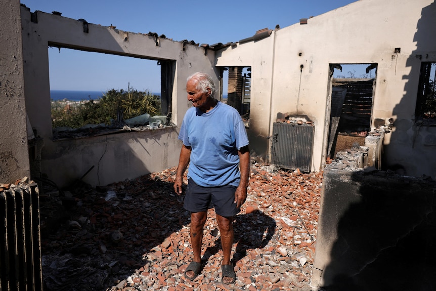 A man stands among the rubble of a burnt-down home. 
