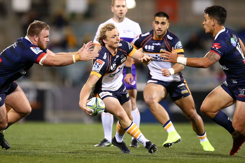 Joe Powell runs with the ball while fending off opposition players.