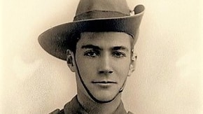 Black and white photo of a young man in military dress, wearing a diggers hat, arms folded. he is smiling and looks in his ear