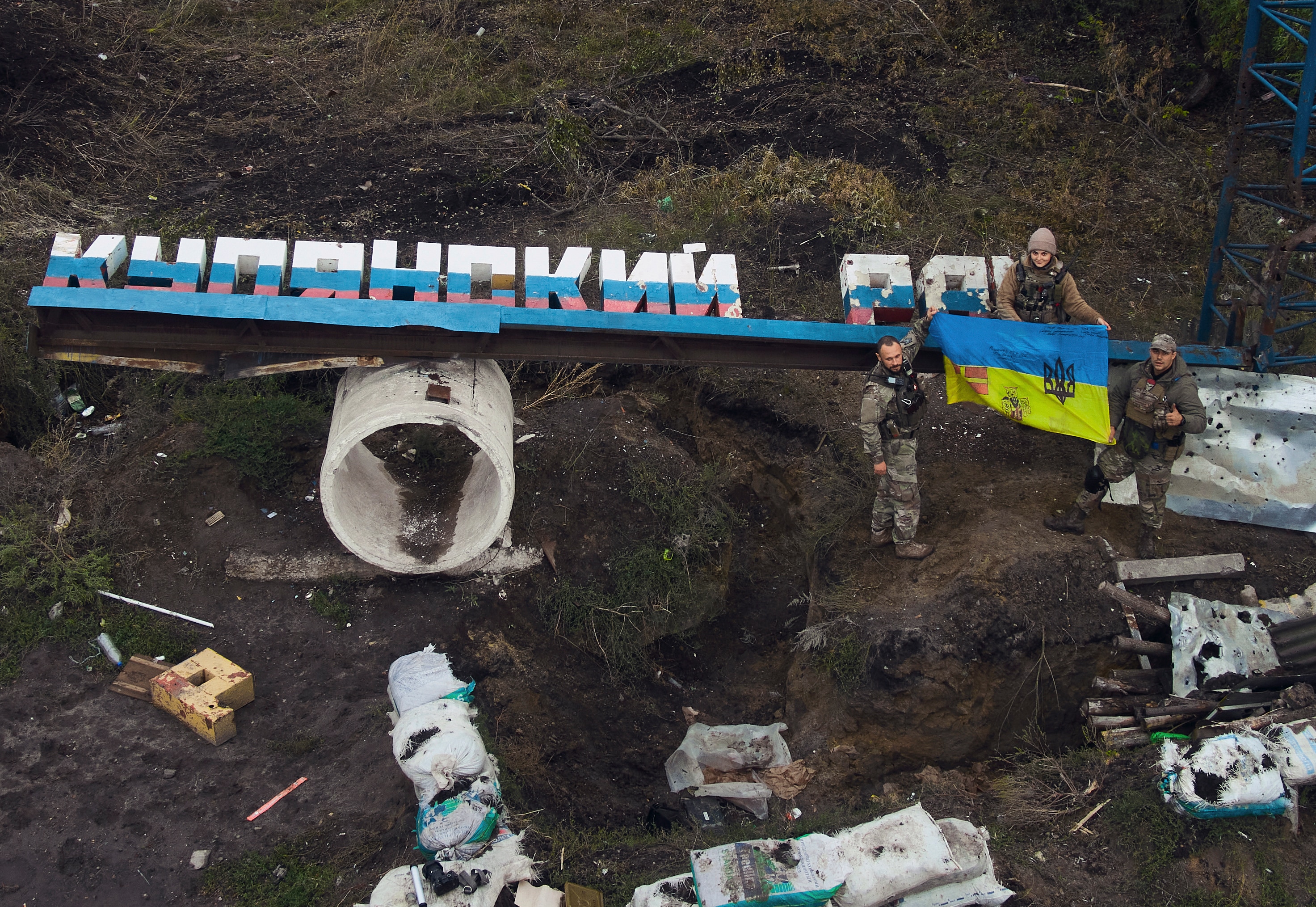 Ukrainian soldiers adjust the national flag on the damaged sign.