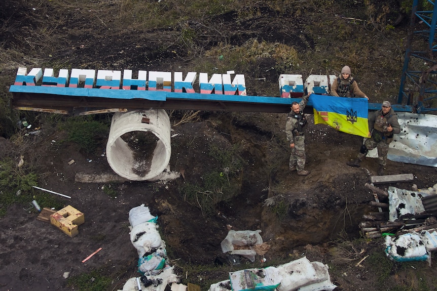 Ukrainian soldiers adjust the national flag on the damaged sign.