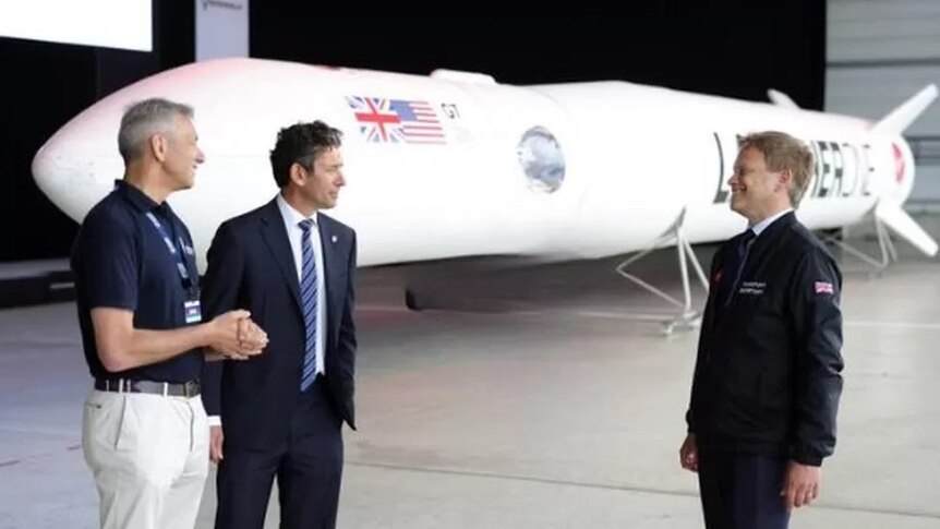 Grant Schapps (right) laughs as he looks across a vast empty space toward two representatives from Spaceport Cornwall