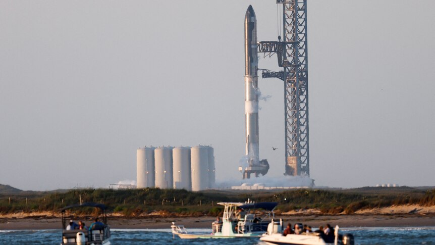 Spectators on small boats in the foreground look towards a huge rocketship ready for launch.