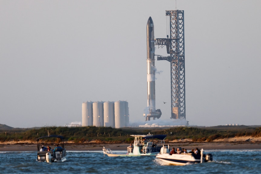 Spectators on small boats in the foreground look towards a huge rocketship ready for launch.