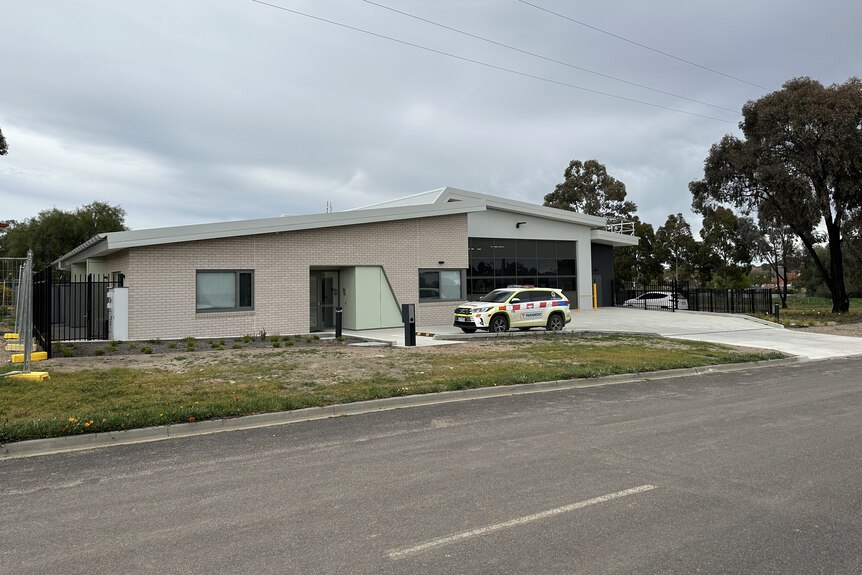 Exterior of new Ambulance station with ambulance vehicle in driveway, overcast sky.