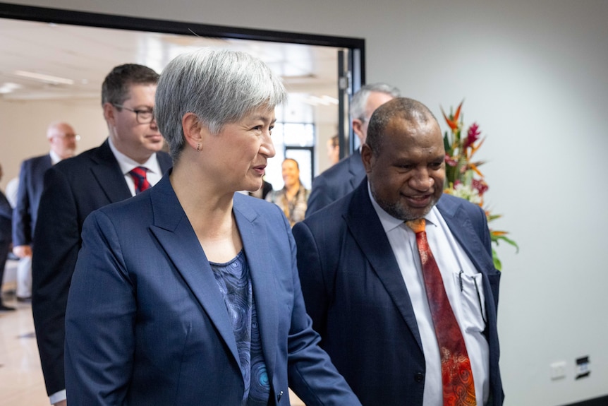 Penny Wong dressed in a dark pantsuit smiles while talking to James Marape dressed in a dark suit and red tie.