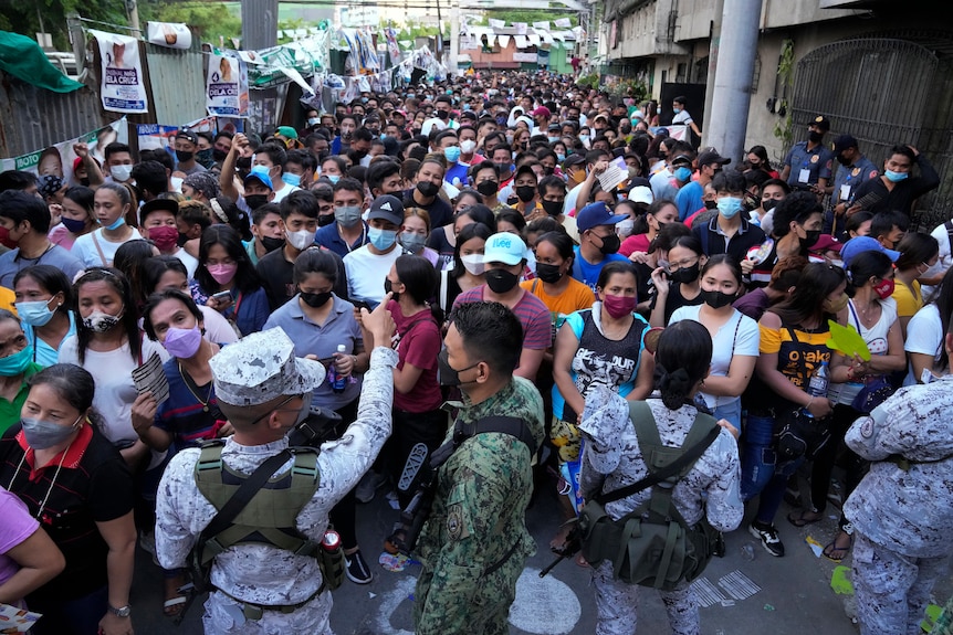 Security forces stand in front of a large crowd at a Manila polling station